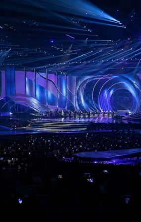 Panggung acara penghargaan musik K-pop dengan pencahayaan biru dan ungu serta penonton di Busan