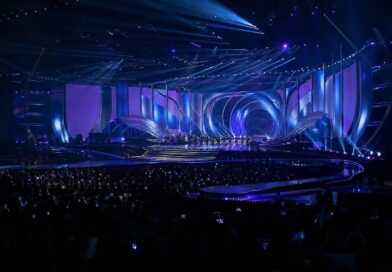 Panggung acara penghargaan musik K-pop dengan pencahayaan biru dan ungu serta penonton di Busan