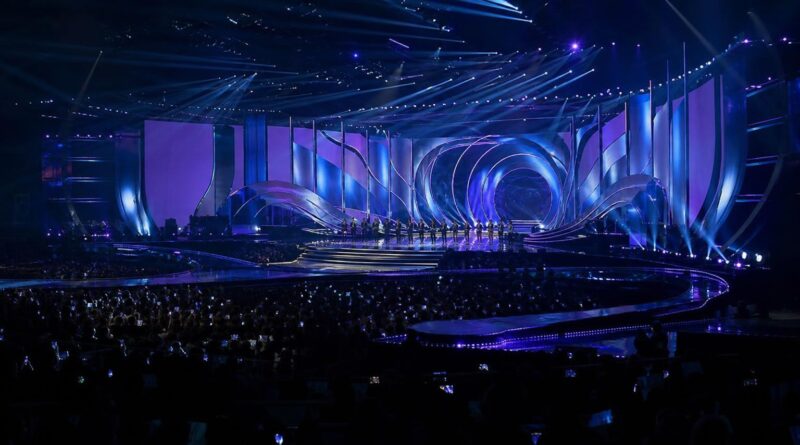 Panggung acara penghargaan musik K-pop dengan pencahayaan biru dan ungu serta penonton di Busan