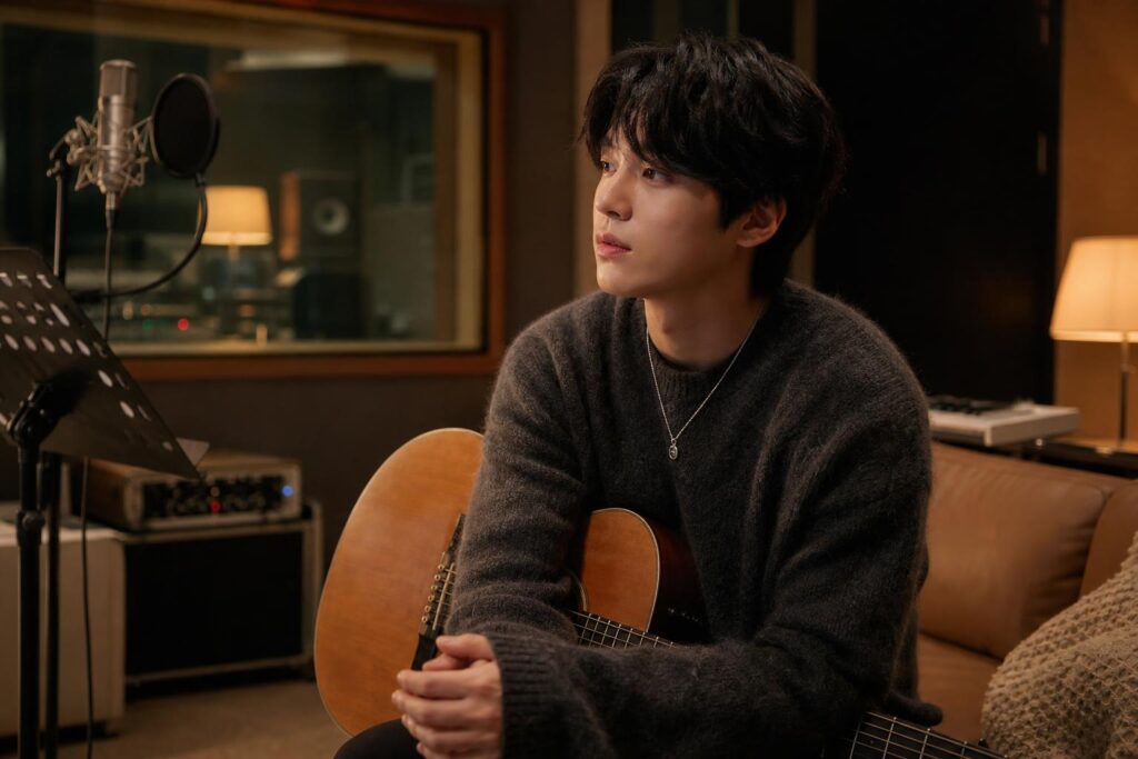 Penyanyi solo duduk di studio rekaman dengan gitar akustik dalam suasana hangat dan tenang