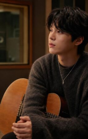 Penyanyi solo duduk di studio rekaman dengan gitar akustik dalam suasana hangat dan tenang