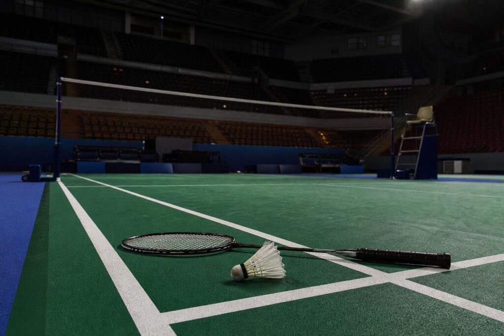 Lapangan bulu tangkis kosong di arena Asian Games dengan raket dan kok di dekat garis lapangan