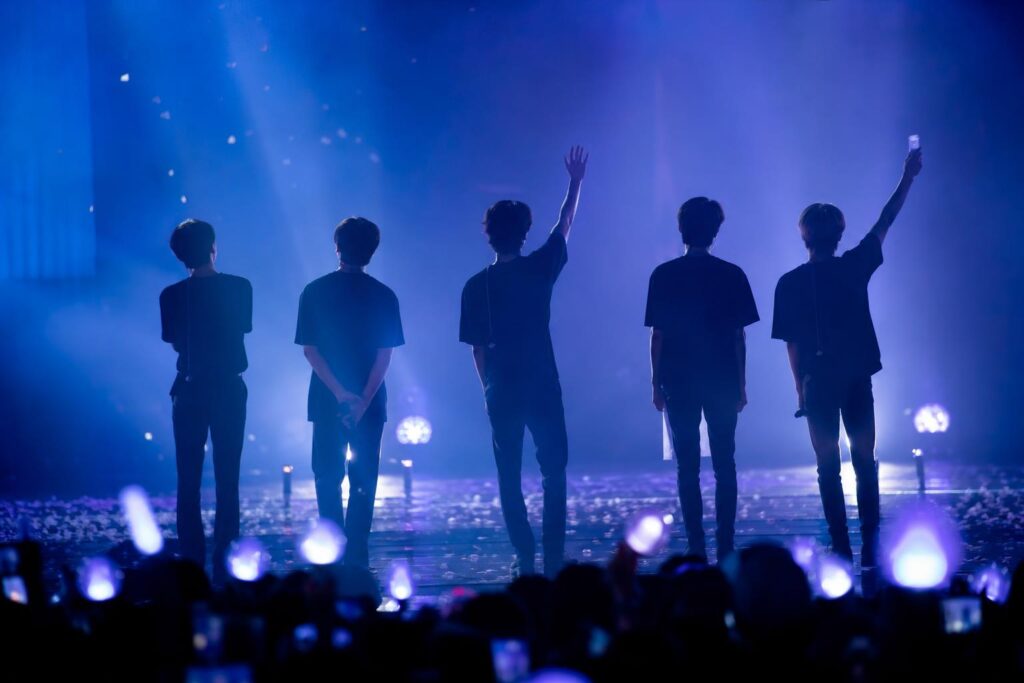 Panggung fan meeting dengan siluet para penampil dan cahaya konser biru-ungu