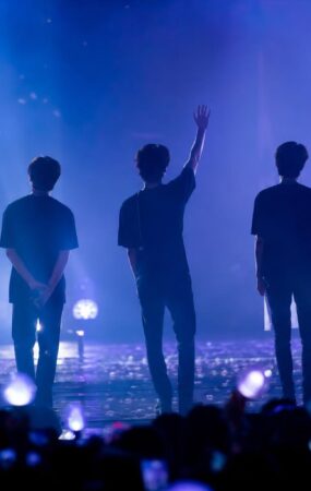 Panggung fan meeting dengan siluet para penampil dan cahaya konser biru-ungu