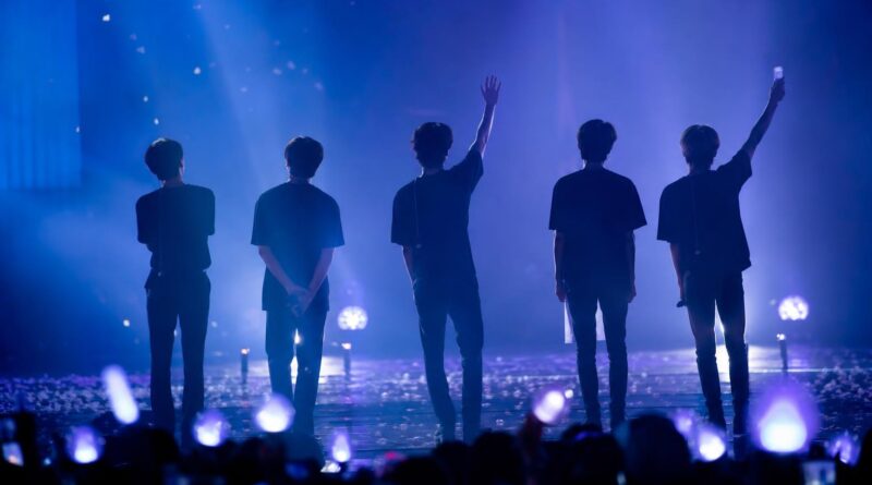 Panggung fan meeting dengan siluet para penampil dan cahaya konser biru-ungu