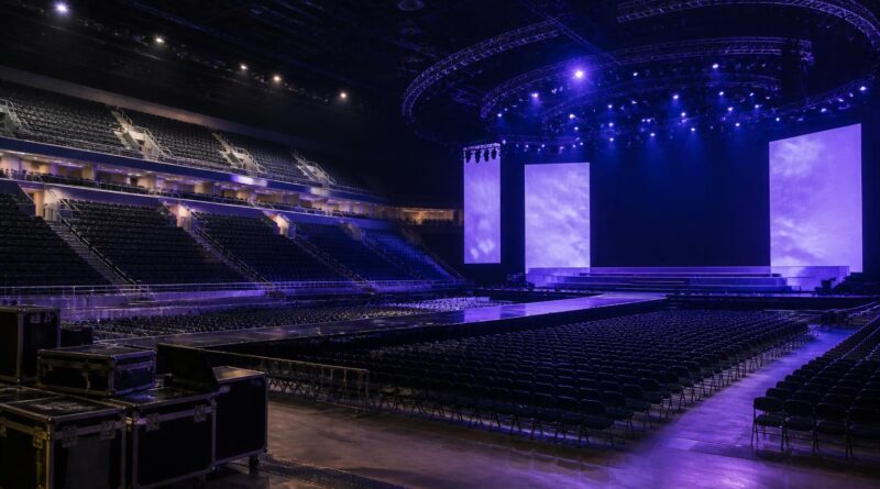 Panggung konser arena yang kosong dengan pencahayaan biru dan ungu serta perlengkapan produksi di sisi belakang