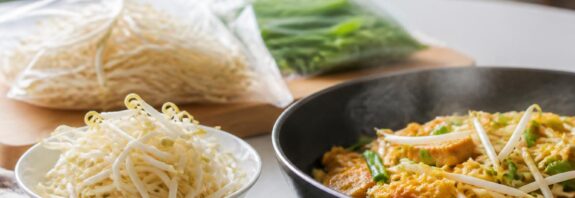 Kecambah segar dalam mangkuk di samping hidangan kecambah yang telah dimasak