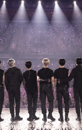 Suasana konser K-pop dengan para penggemar memegang cahaya ungu dan panggung yang diterangi lampu