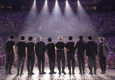 Suasana konser K-pop dengan para penggemar memegang cahaya ungu dan panggung yang diterangi lampu