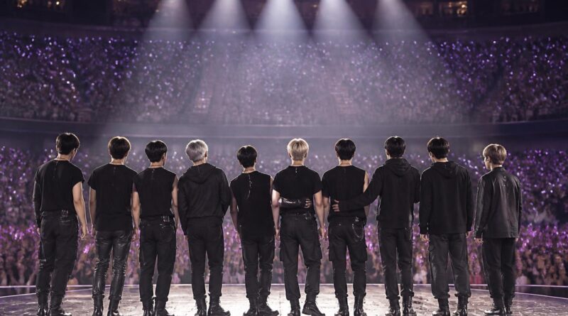 Suasana konser K-pop dengan para penggemar memegang cahaya ungu dan panggung yang diterangi lampu
