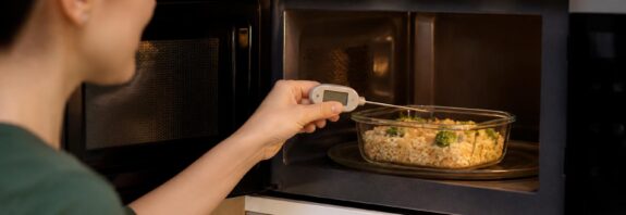 Wadah makanan sisa dipanaskan di dapur dengan termometer makanan untuk memeriksa suhu internal