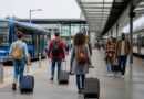 Wisatawan membawa ransel menunggu transportasi umum di area stasiun yang tertata