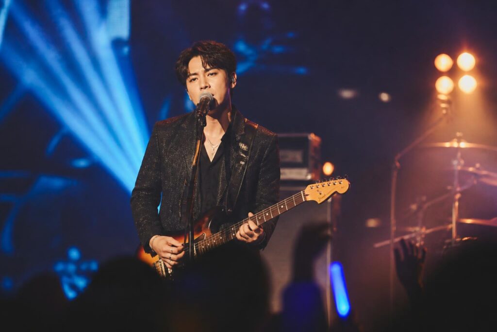 Penyanyi solo tampil di panggung konser dengan pencahayaan biru dan amber serta siluet penonton
