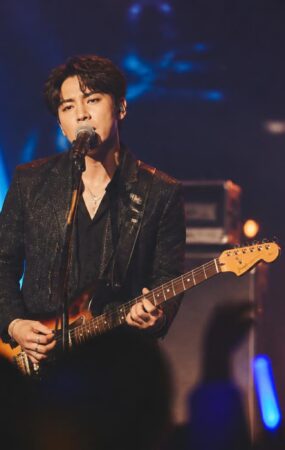 Penyanyi solo tampil di panggung konser dengan pencahayaan biru dan amber serta siluet penonton