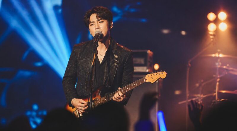 Penyanyi solo tampil di panggung konser dengan pencahayaan biru dan amber serta siluet penonton