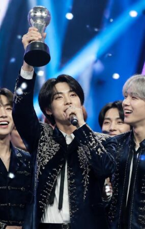 Grup K-pop merayakan kemenangan lagu terbaru mereka di atas panggung acara musik dengan trofi dan konfeti.