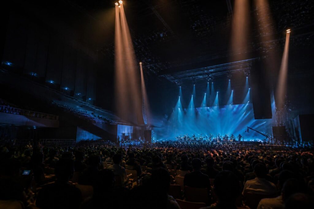 Suasana konser musik di arena Seoul dengan panggung bercahaya dan penonton dari belakang