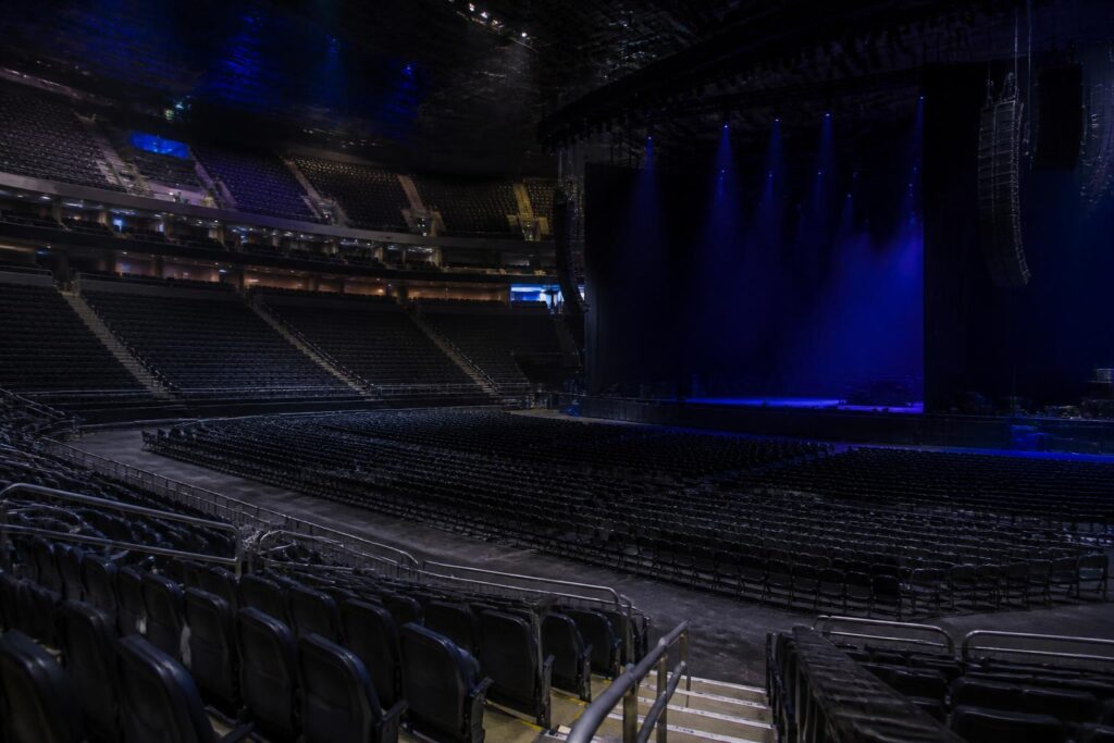 Panggung arena konser yang kosong dengan pencahayaan biru dan deretan kursi tanpa penonton
