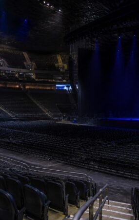 Panggung arena konser yang kosong dengan pencahayaan biru dan deretan kursi tanpa penonton