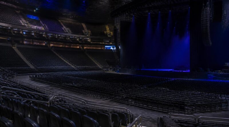 Panggung arena konser yang kosong dengan pencahayaan biru dan deretan kursi tanpa penonton