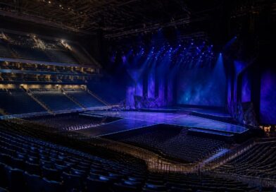 Panggung konser di arena dalam ruangan dengan pencahayaan biru dan ungu serta deretan kursi penonton yang kosong