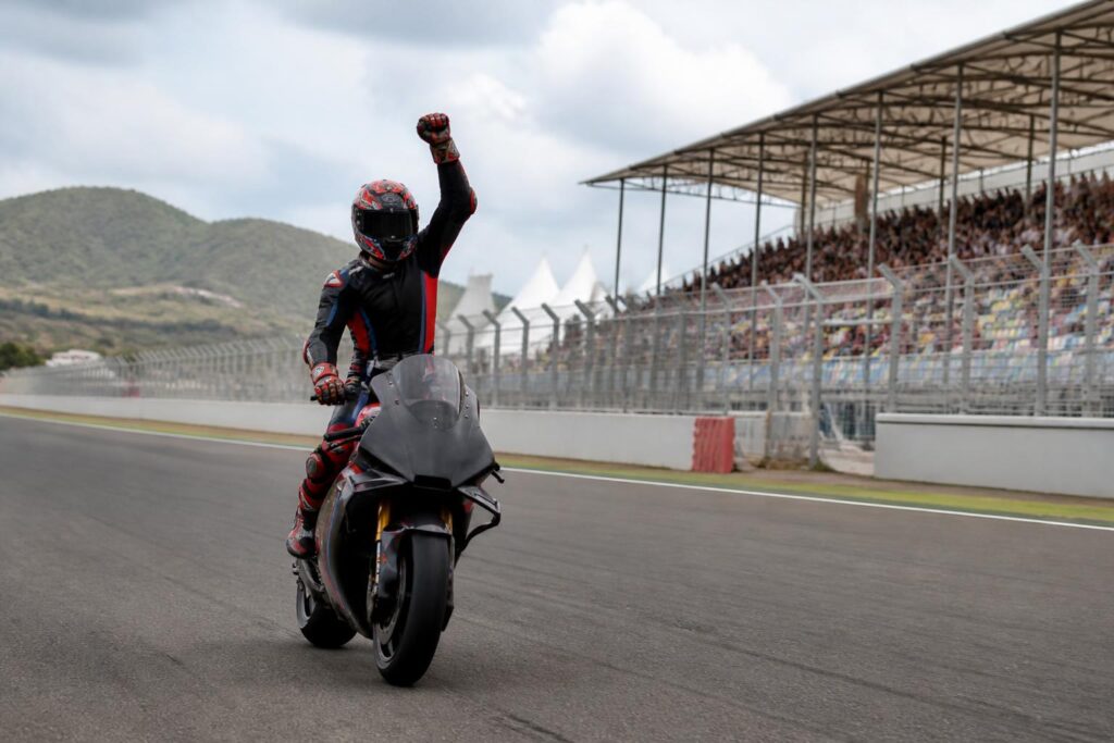 Pembalap motor merayakan kemenangan sprint di lintasan Mandalika dengan tribun sirkuit terlihat di belakangnya