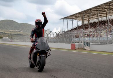 Pembalap motor merayakan kemenangan sprint di lintasan Mandalika dengan tribun sirkuit terlihat di belakangnya