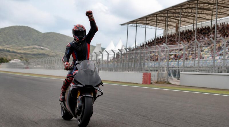 Pembalap motor merayakan kemenangan sprint di lintasan Mandalika dengan tribun sirkuit terlihat di belakangnya