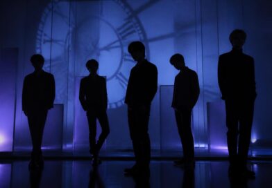 Siluet sekelompok performer dalam suasana studio bernuansa biru dan ungu yang menggambarkan hitung mundur comeback musik