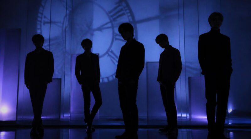 Siluet sekelompok performer dalam suasana studio bernuansa biru dan ungu yang menggambarkan hitung mundur comeback musik