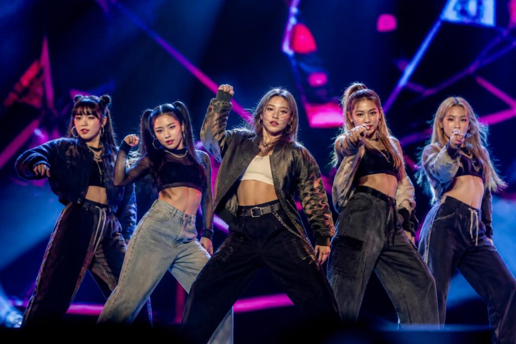 Grup perempuan K-pop tampil dengan koreografi energik di atas panggung dalam suasana konser tur internasional