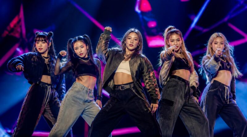 Grup perempuan K-pop tampil dengan koreografi energik di atas panggung dalam suasana konser tur internasional